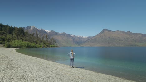 Female-hiker-arriving-at-Wilson-Bay-with-stunning-view-of-calm-lake,-New-Zealand