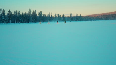 Snowmobile-riders-driving-across-snowy-Lapland-woodland-towards-camera-at-sunrise