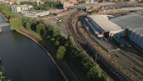 Aerial-Drone-Shot-of-River-Ouse-and-National-Railway-Museum-with-Train-Passing-Through-Entering-York-Railway-Station-on-Sunny-Sunset-Evening-with-Trees-and-Footbridge-North-Yorkshire-United-Kingdom