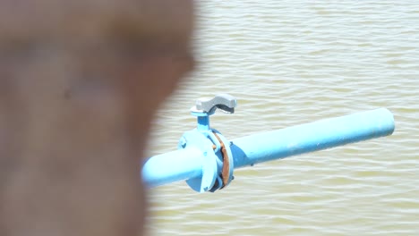 Dolly-Right-Reveal-Of-Blue-Water-Pipe-With-Outflow-Pipe-Beside-Body-Of-Water