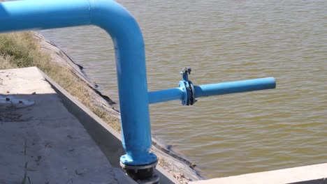 Blue-Water-Pipe-With-Outflow-Pipe-Beside-Body-Of-Water