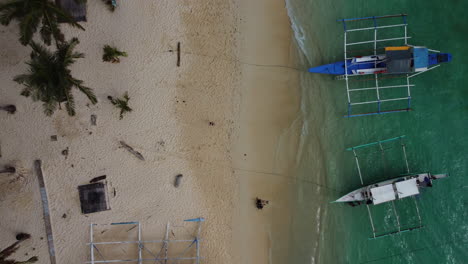 Top-view-drone-shot-pulling-away-from-tropical-beach-with-palm-trees-and-boats