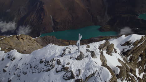 Aerial-birds-eye-shot-of-cross-on-summit-with-green-lake-in-valley-in-winter---Zell-am-See,Austria