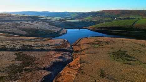 Aerial-footage-flying-over-golden-moorlands-and-around-a-bue-lake,-reservoir-in-the-distance