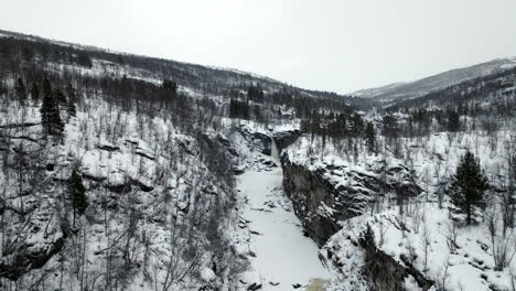 Aerial-over-snowy-winter-wilderness---frozen-river-and-falls-in-canyon