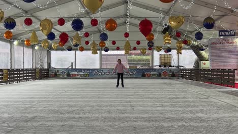 Little-girl-skating-on-ice-alone-in-empty-indoor-ice-rink-with-Christmas-decorations