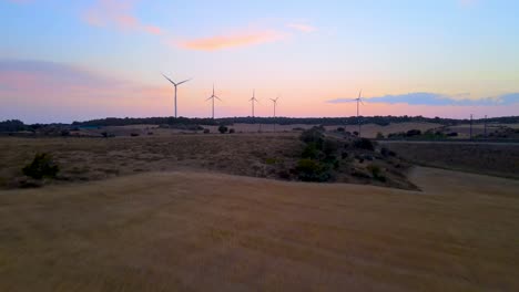 Große-Windkraftanlagen-Im-Weizenfeld-Luftbild-Leuchtend-Orangefarbener-Sonnenuntergang-Blauer-Himmel-In-Der-Spanischen-Landschaft-Mit-Ave-Hochgeschwindigkeitsbahn