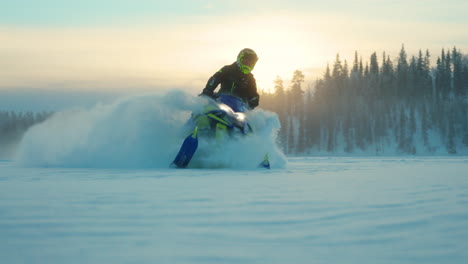 Rider-on-snowmobile-leaving-snowy-powder-trail-driving-on-arctic-circle-woodland-landscape-at-sunrise