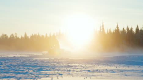 Snowmobile-rider-driving-across-glowing-sunrise-snowy-Swedish-alpine-forest,-Slow-motion