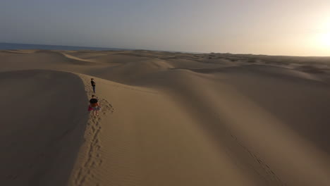 Aerial-circling-unrecognizable-people-on-top-of-sand-dune-at-sunset,-Maspalomas