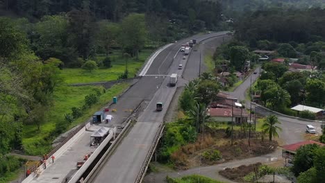 Trucks-and-cars-crossing-bridge-under-construction-over-river-affected-by-drought-in-San-Jose,-Costa-Rica,-Aerial-pan-right-reveal-shot