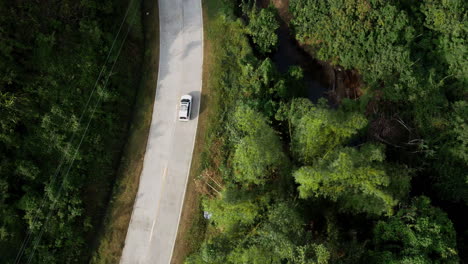 Aerial-view-following-white-car-on-paved-road-driving-through-tropical-forest