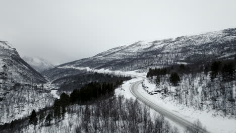 Aerial-along-Highway-E8-through-white-snow-covered-winter-landscape,-Norway