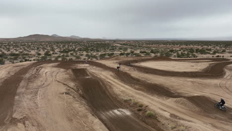 Motorcyclists-racing-on-a-off-road-racetrack-and-making-long-jumps-off-dirt-ramps-in-slow-motion---aerial-view