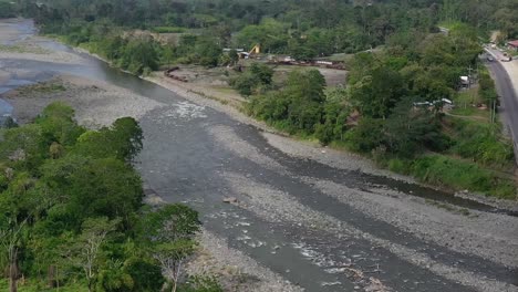 Trucks-crossing-bridge-under-construction-over-river-affected-by-drought-in-San-Jose,-Costa-Rica,-Aerial-pan-left-reveal-shot