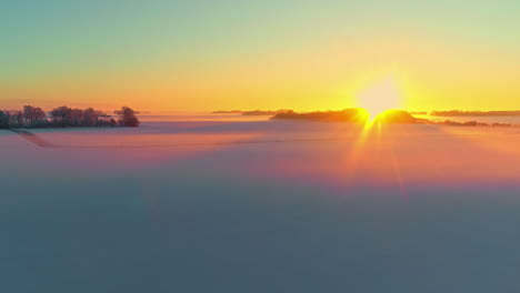 The-sun-sets-on-the-horizon-and-glows-on-the-snowy-fields-of-a-winter-landscape---aerial-view