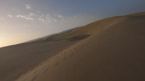 Aerial-fast-low-flight-over-sea-water-towards-sand-dunes-at-sunset,-Maspalomas