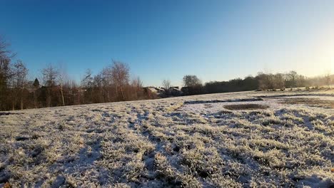 FPV-flying-through-wooden-posts-over-snowy-winter-meadow-towards-glowing-sunlit-sunrise