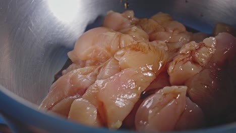 Seasoning-chopped-fresh-raw-chicken-on-a-bowl-and-mixing-it-all-with-a-wooden-spoon,-close-up-view