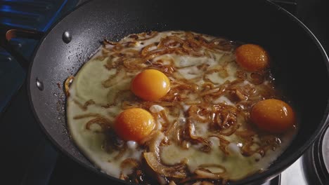 Mixing-fried-eggs-and-onion-in-a-frying-pan-using-a-wooden-spoon,-close-up-view-in-home-kitchen