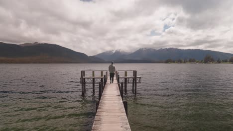 Man-walks-on-wooden-jetty-at-Lake-Te-Anau-in-New-Zealand