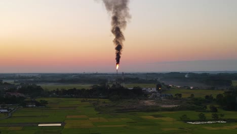 Aerial-view-of-gas-burning-fire-from-pipe-at-a-gas-plant-beside-farmland