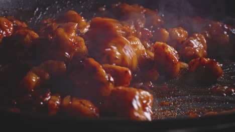 Mixing-sweet-and-sour-chicken-with-sauce-in-a-frying-pan-using-a-wooden-spoon,-close-up-view