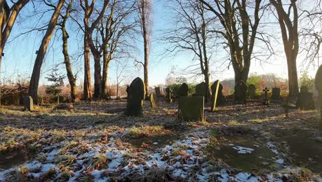 FPV-low-angle-flying-around-sunlit-frosty-winter-gravestones-and-bare-trees-with-sunrise-flares