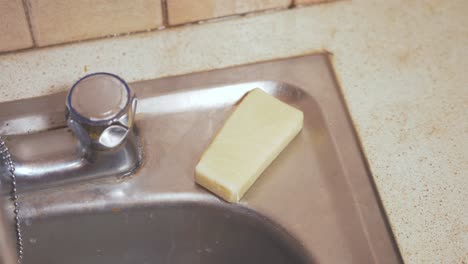 Natural-soap-bar-being-placed-back-at-the-edge-of-sink