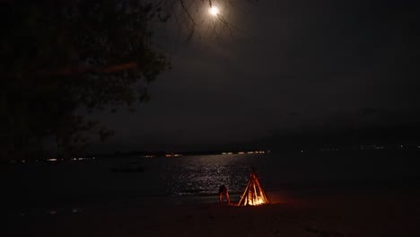 Bonfire-on-the-beach-under-the-full-moon-reflected-on-the-Sea,-tropical-Komodo-Travel-Destination-in-Indonesia