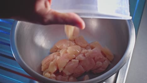 Dropping-raw-chicken-pieces-into-a-bow-in-home-kitchen