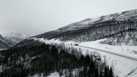 Isolated-truck-driving-along-E8-highway-in-winter-season-with-valley-shrouded-in-mist-on-background,-Norway