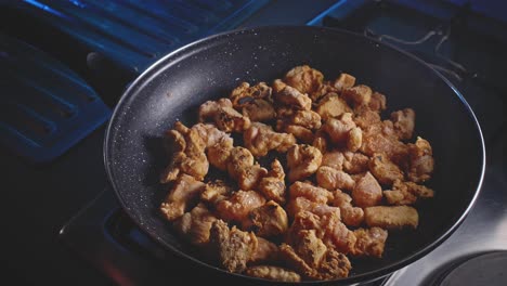 Mixing-floured-and-seasoned-pieces-of-chicken-in-a-frying-pan-using-a-wooden-spoon,-close-up-view