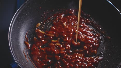 Pouring-broth-into-a-frying-pan-with-chopped-onion-and-tomato-sauce-being-cooked,-close-up-view