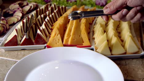 Close-up-of-person-serving-on-plate-slices-of-delicious-cheese-from-a-tray-with-a-variety-of-them