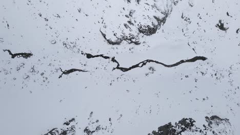 Drohnenaufnahmen-Von-Oben-Nach-Unten-Von-Einem-Zugefrorenen-Fluss-In-Schneebedeckten-Bergen
