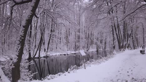 Cold-snowy-river-with-gentle-snowfall-along-frosty-riverbank-winter-landscape-pathway