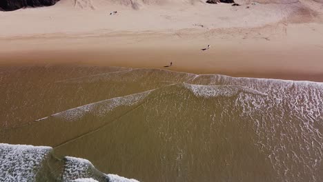 A-view-from-above-of-some-people-and-surfers-walking-along-the-beach-in-Algarve,-Portugal