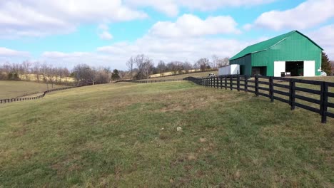 Aerial-moving-down-a-fence-row-on-a-horse-farm-in-Kentucky-with-a-large-green-barn-on-the-right-bluegrass-state