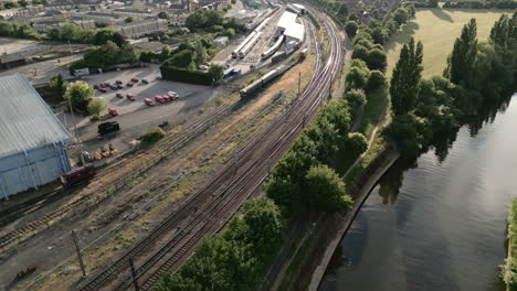 Panning-Aerial-Drone-Shot-Looking-Down-York-Railway-Line-next-to-the-National-Railway-Museum-with-Diesel-Trains-Parked-at-Sunset-with-Trees-and-Parked-Cars
