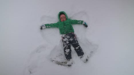 Young-Boy-Making-Snow-Angels-While-Snow-Gently-Falls,-Slow-Motion
