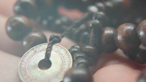 A-wooden-beads-necklace-with-an-old-Asian-coin-in-a-man-hand,-Macro-shot,-4K