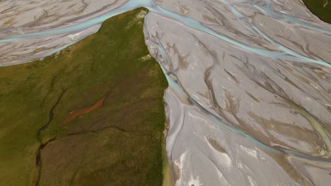 Aerial-shot-revealing-epic-snow-capped-mountain-range-behind-a-glacier-river-delta-with-turquoise-water-feeding-lake-tekapo