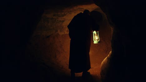 El-Hombre-Monje-Está-Entrando-En-Una-Cueva-Oscura-Mientras-Sostiene-Un-Concepto-De-Ermitaño-A-La-Luz-De-Las-Velas,-Misterioso-Y-Religioso