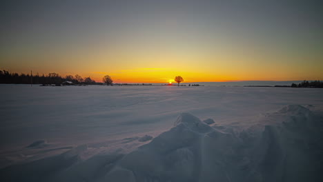 Time-lapse-wide-shot-of-golden-sunrise-at-horizon-lighting-on-snowy-white-winter-landscape-field