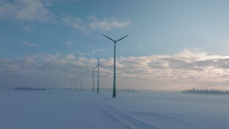 Luftaufnahmen-Von-Windkraftanlagen,-Die-Im-Windpark-Erneuerbare-Energie-Erzeugen,-Schneebedeckte-Landschaft-Mit-Nebel,-Sonniger-Wintertag,-Weit-Aufsteigende-Drohnenaufnahme,-Die-Sich-Vorwärts-Bewegt