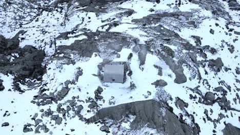 Top-down-rocket-like-drone-footage-of-a-refuge-on-a-cliff-in-snow-mountains