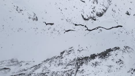 Drohnenaufnahmen-Von-Oben-Nach-Unten-Eines-Zugefrorenen-Flusses-In-Schneebedeckten-Bergen,-Nach-Rechts-übersetzt