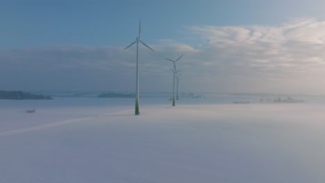 Luftaufnahmen-Von-Windkraftanlagen,-Die-Im-Windpark-Erneuerbare-Energie-Erzeugen,-Schneebedeckte-Landschaft-Mit-Nebel,-Sonniger-Wintertag,-Weit-Aufsteigende-Drohnenaufnahme,-Die-Sich-Vorwärts-Bewegt