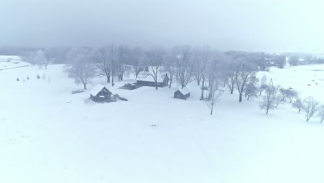 Aerial-flyover-snowy-winter-landscape-and-snow-covered-farm-house-in-countryside---tilt-down